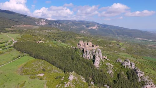 Lateral drone shot of medieval hilltop castle surrounded by forest and rural mountain landscape in S