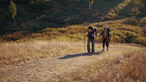 Pareja de excursionistas sube cuesta arriba apoyándose en bastones de marcha nórdica