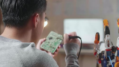 Over The Shoulder View Of A Male Holding And Fixing The Board While Repairing A Cyborg Hand At Home