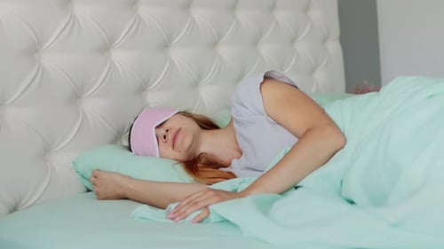 Uma jovem dorme com uma máscara de dormir em uma cama grande em um quarto modernamente renovado