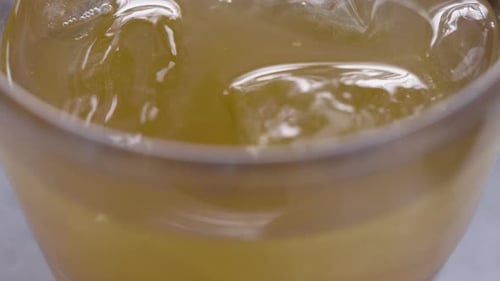 Panning shot of orange drink in glass with ice and straw. Extreme close up.
