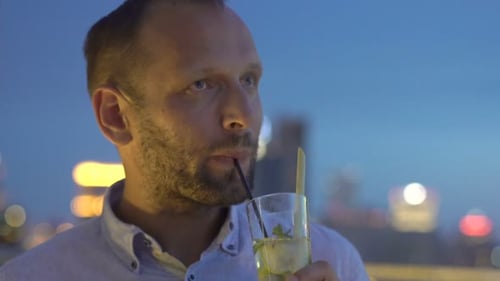 Man Relaxing And Drinking Cocktail Sitting On Terrace In Bar At Night