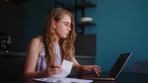 Young Adult Woman Works on Laptop and Paperwork