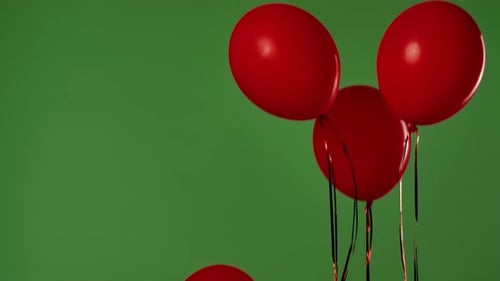Four Red Helium Balloons with Shiny Ribbons Float Upward Against a Green Background with a Chroma