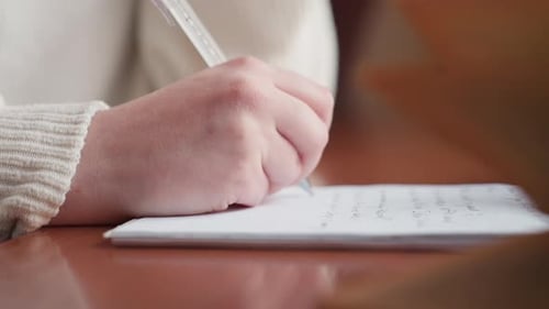 Extreme Close Up of Hand Writing on Notebook with Blurred Open Book in Foreground
