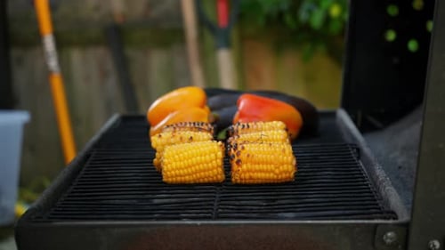 Ein Stück Mais auf dem Grill grillen Ein Mann verwendet eine Metallzange, um Mais von einem Metallgrill zu entfernen