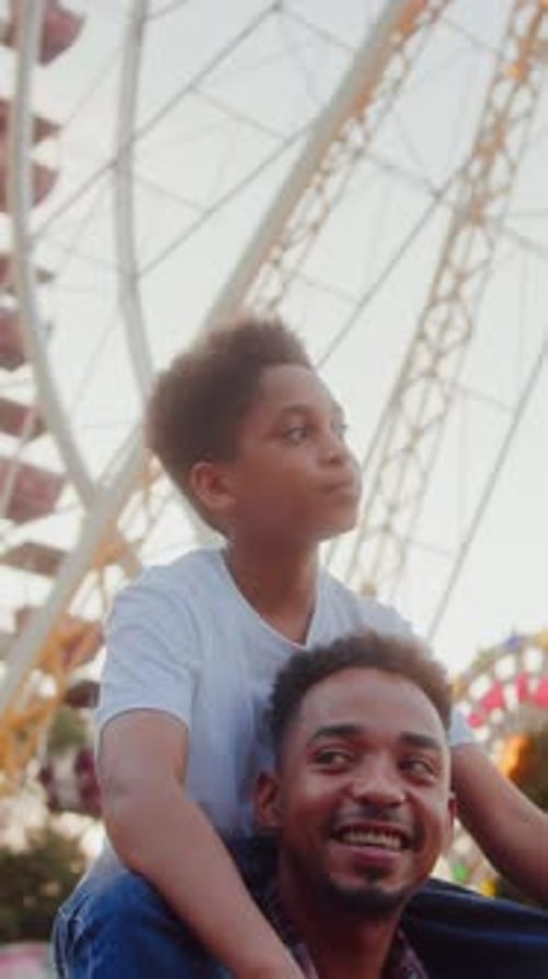 Man Giving Son Piggyback Ride While Passing By Ferris Wheel