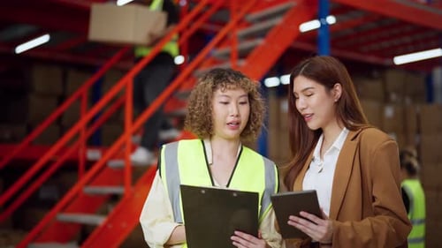 Female warehouse manager and worker reviewing inventory details