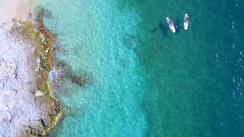 Aerial view of two people paddleboarding in clear ocean