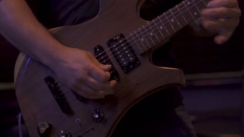 Man strumming strings on a guitar in a low light venue in 4K Medium Shot