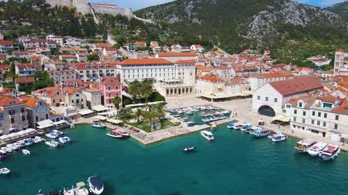 Panorama einer Küstenstadt mit vielen Häusern mit roten Dächern, umgeben von Meer und Bergen mit