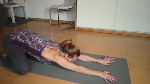 A woman at home stretches and lowers herself into a yoga pose on her mat, then raises up again. 4K.