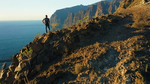 Hiker Man with Backpack on Edge of Sheer Cliff Overlooking Ocean