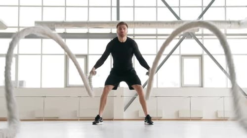 Athletic Man Exercising With Battle Ropes in Gym