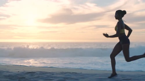Sporty, active and athletic woman running, training and exercising on the beach shore during sunset