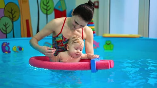 Baby boy holding by the pool foam in the swimming pool.