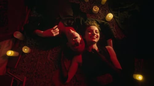 Smiling Vampire Lovers Lying on Patterned Rug Among Glow of Numerous Lit Candles