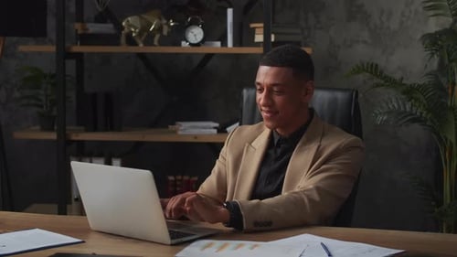Smiling Male Businessman Sits in the Office and is in Correspondence with Business Partners A Young