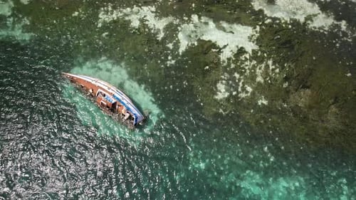 Ein zerstörtes Segelboot liegt halb versunken in kristallklarem türkisfarbenem Wasser in der Nähe einer üppigen Küste