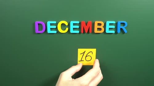 Hand sticking a sticker 16 December calendar day on school board. 16 date of December. Sixteenth