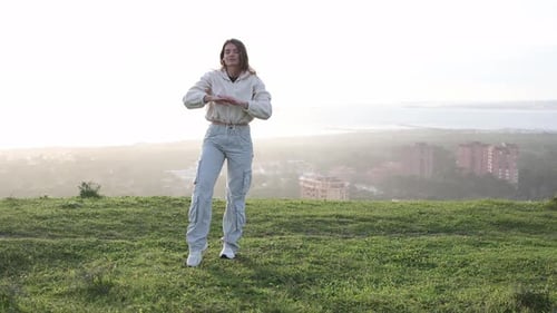 Woman Dancing on Grassy Hill Overlooking City