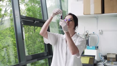 Laboratory worker holding blood sample in test tube near window, middle shot, front view