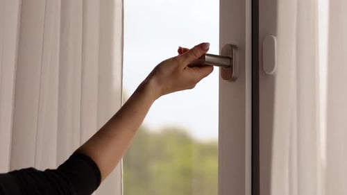A person reaches for the window handle to open it, inviting fresh air into the cozy room.