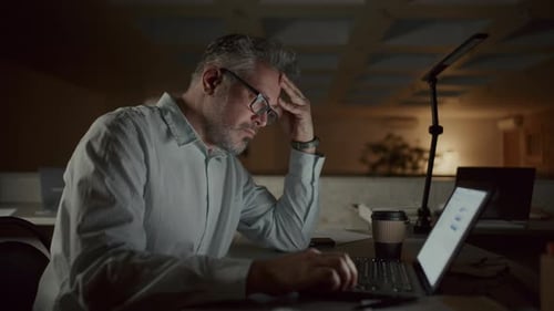 Empresário sênior se sentindo sobrecarregado por trabalhar até tarde sozinho no escritório