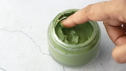 Finger scooping green cream from glass jar