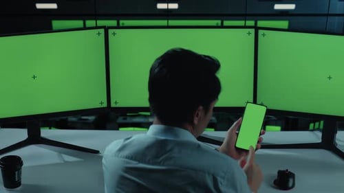 Asian Man Using Mobile Phone And Multiple Computer Monitor With Mock Up Green Screen In office