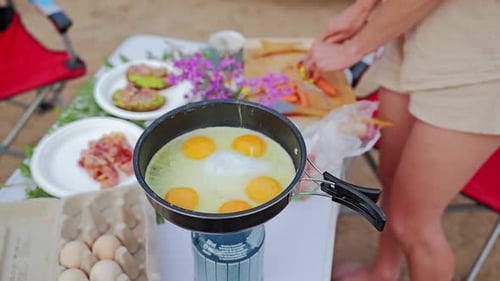 Cooking eggs in frying pan on portable stove during outdoor breakfast prep