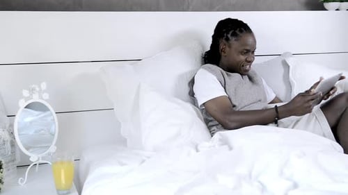 Man Smiling Using Tablet While Relaxing in Bed