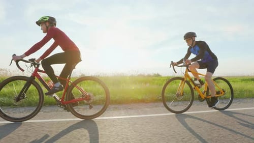 Side View of Two Cyclists Riding on Paved Road