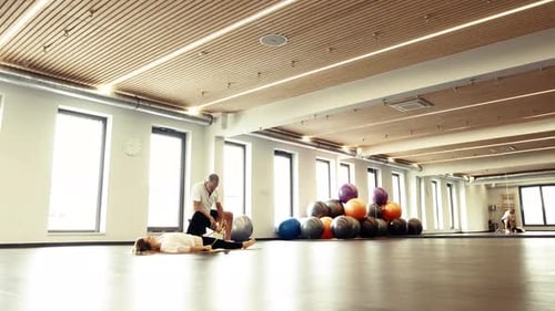 Trainer Assists Woman Stretching in Bright Gym Studio
