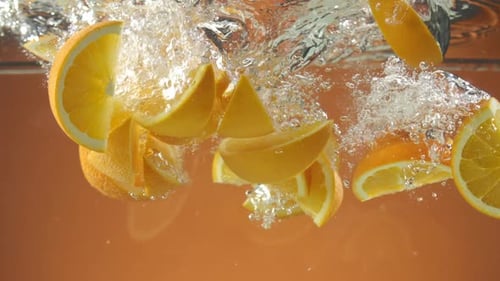Slow motion of fresh sliced Oranges falling into water on orange background