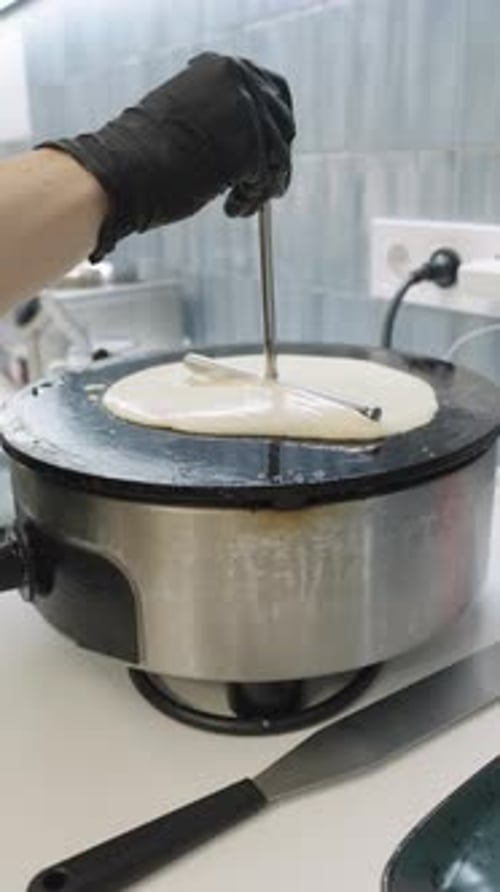 Le chef étale la pâte à crêpes sur une plaque chauffante