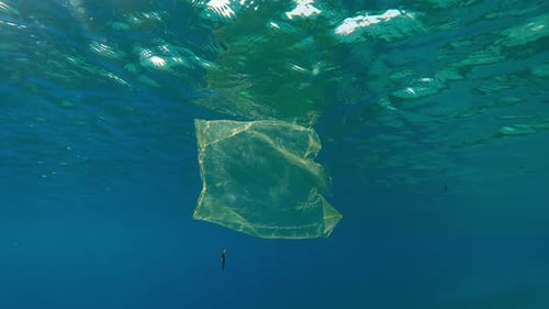 Plastic pollution of Ocean, Old yellow plastic bag drifting below water reflected on surface