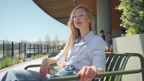 Femme adulte portant des lunettes assise sur une chaise métallique en plein air, café, terrasse