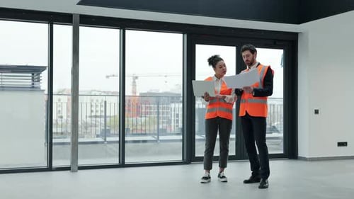 Businessman and Businesswoman Discussing Blueprints in a New Office Building