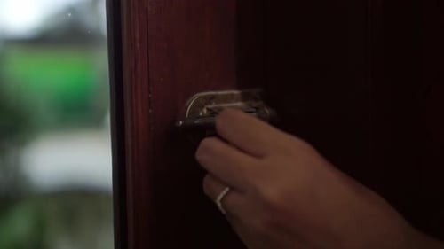 Human hand turning a door lock on a wooden door.