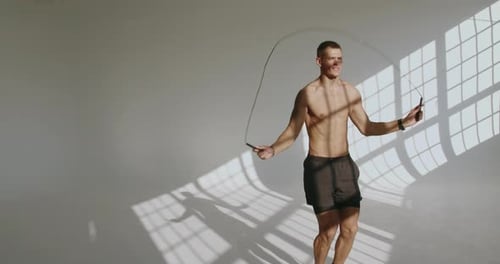 Junger athletischer Mann springt im sonnenbeschienenen Studioraum