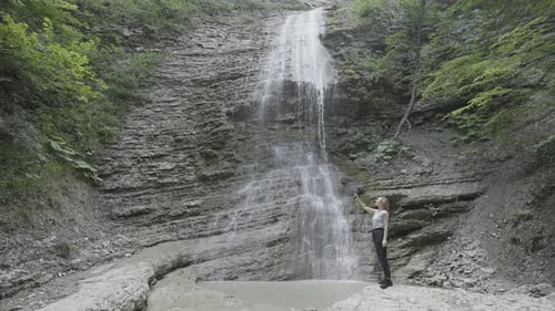 Woman Taking Pictures or Shooting Video of Mountains and Waterfall on Her Smartphone Using a Tripod