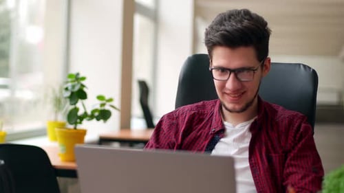 Young Adult Man Works on Laptop in Bright Office