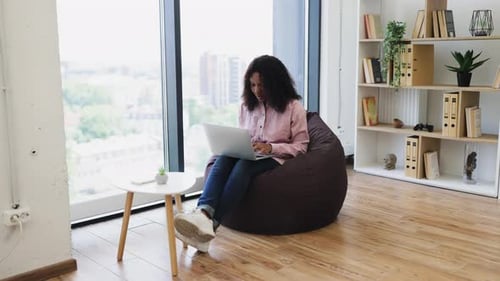 Woman works on laptop sitting in comfortable beanbag chair