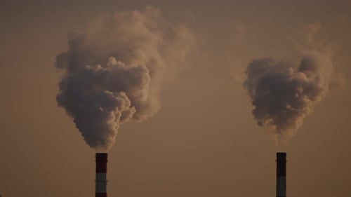 Industrial Smokestacks Billowing Smoke Against Orange Sky