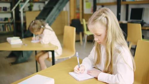 Ein Grundschulmädchen macht Klassenarbeiten in ihrem Notizbuch und fragt ihre Klassenkameradin ein anderes Mädchen