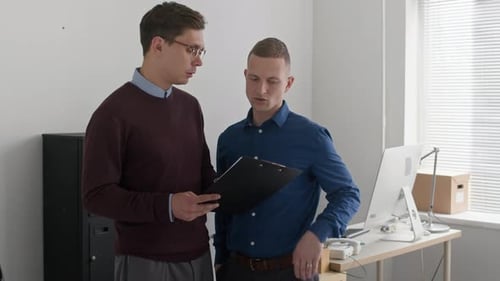 Two Male Colleagues Discussing Document while Working at Office