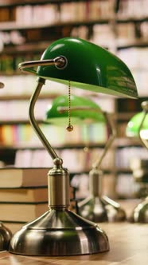 Vertical Video Close Up View of Stack of Books Near Green Lamps on Wooden Library Table