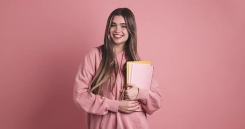 Cheerful Young Woman Holding Books in Pink Studio