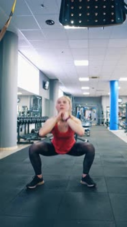 Young woman is squatting in the gym.